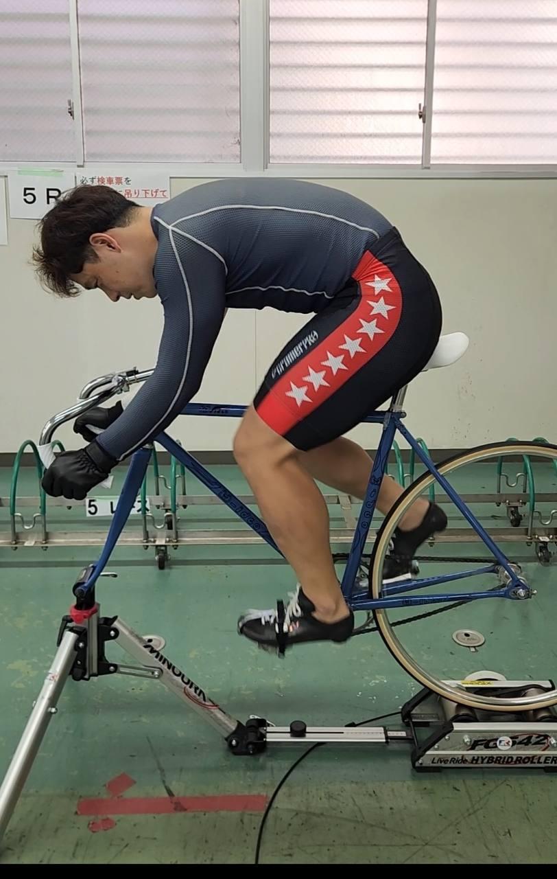 ローラー台に固定した青い競輪自転車で、前傾した乗車姿勢を確認する様子