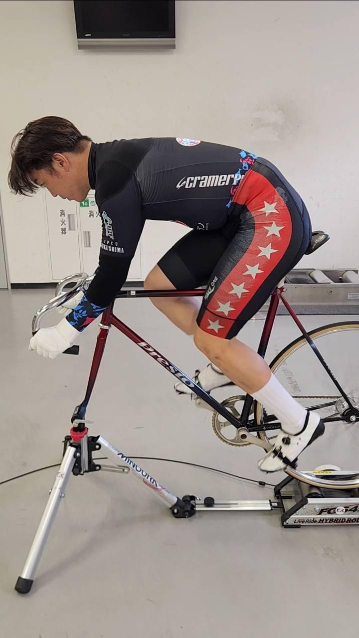 ローラー台に固定した赤い競輪自転車に乗り、横から乗車姿勢を確認する様子