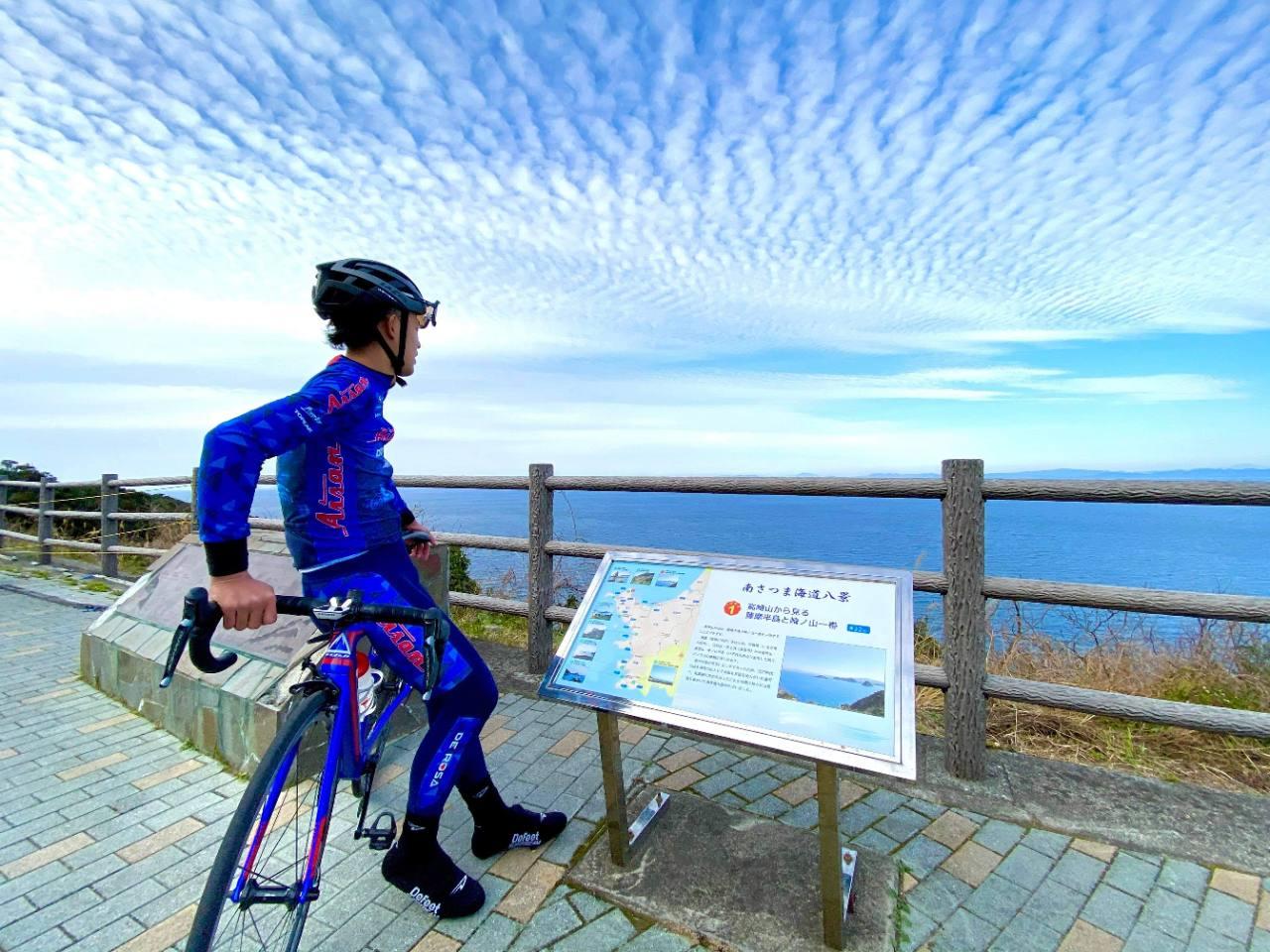 青いサイクルウェアでロードバイクとともに海を眺めるサイクリスト