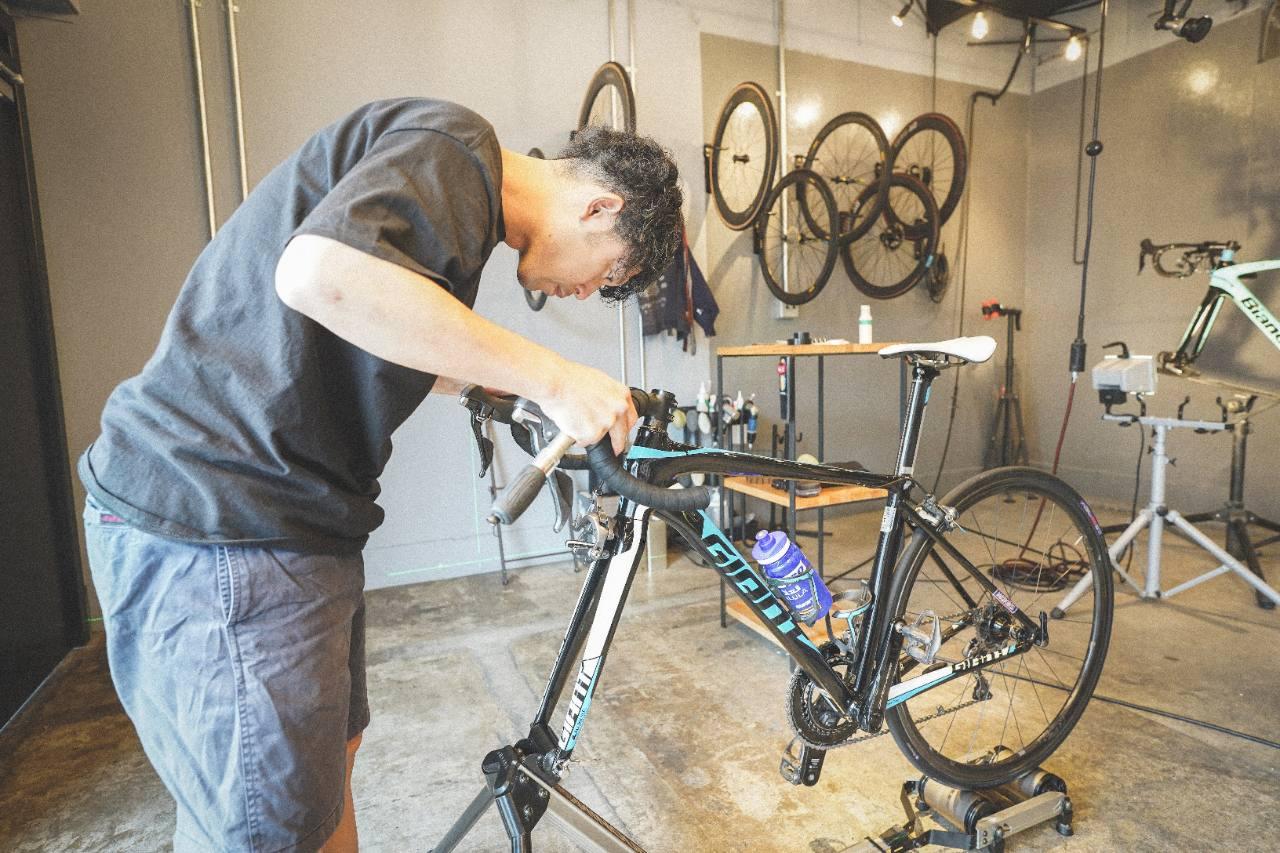 ローラー台に固定したロードバイクのハンドル周辺を確認するフィッティング作業の様子