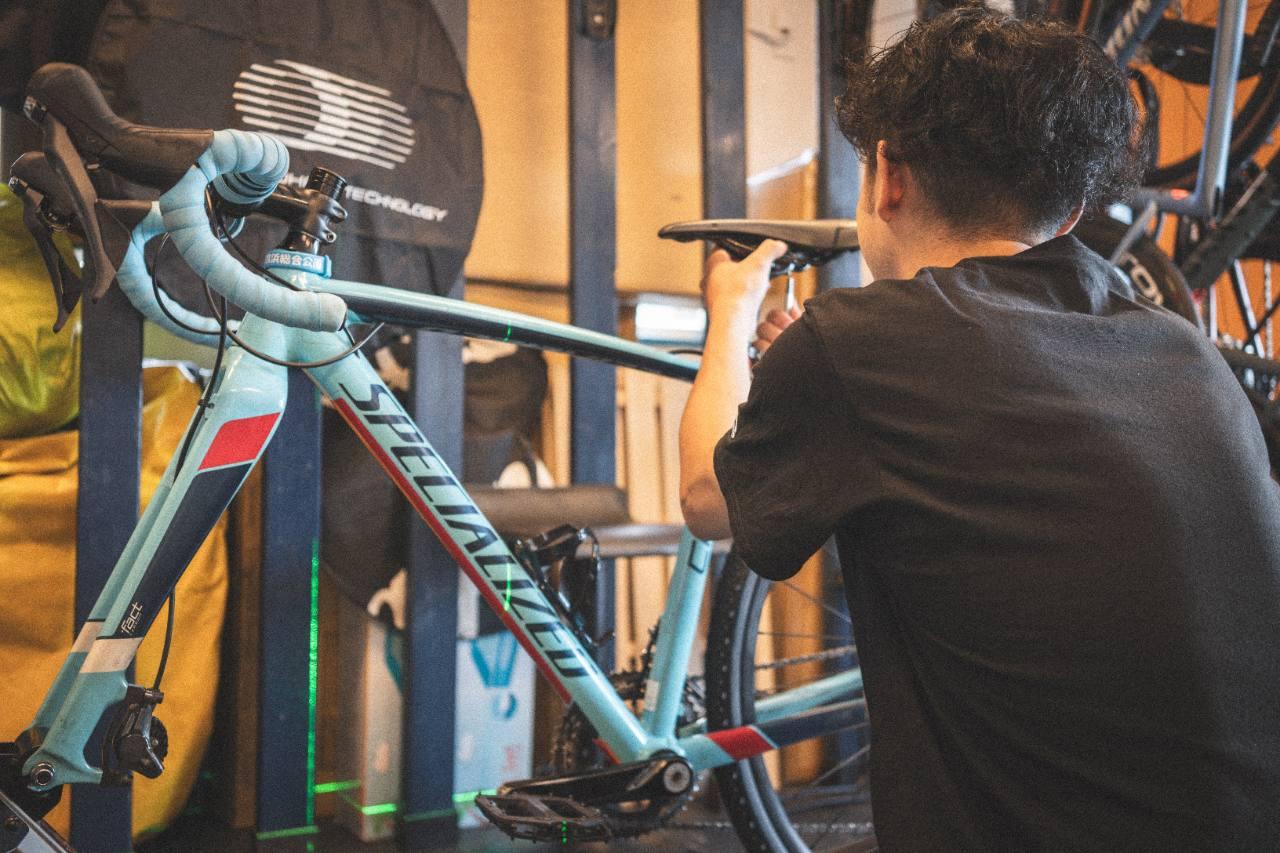 ロードバイクの横にしゃがみ、工具を使ってサドル周辺を調整している様子